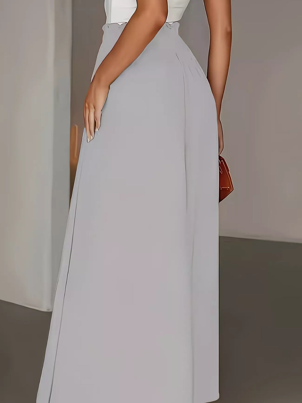 Person wearing a long light gray skirt with a white top against a neutral background