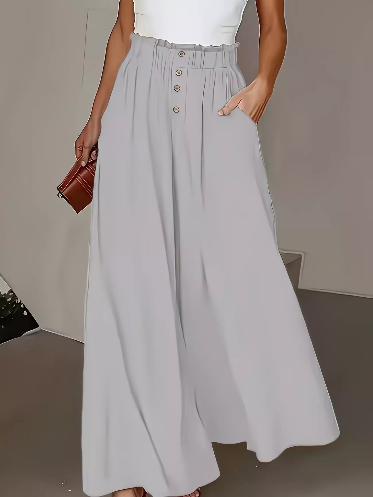 Person wearing light gray wide-leg pants with a white top and brown clutch against a neutral background