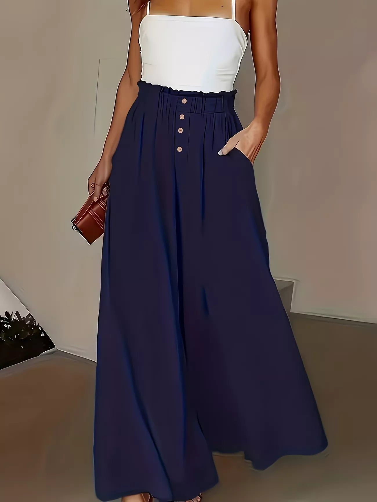 Person wearing a white top and navy blue wide-leg pants holding a brown clutch.