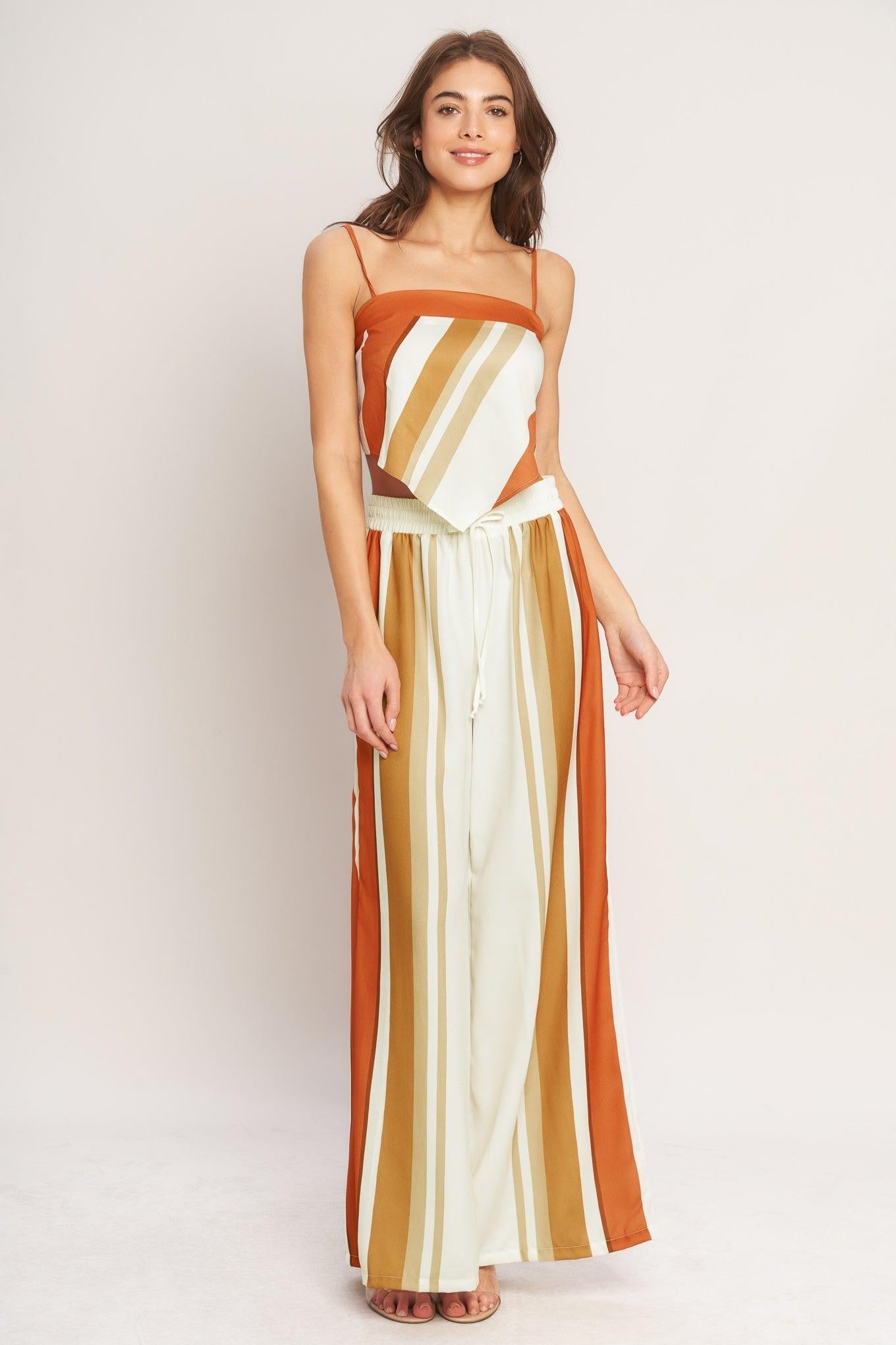 Woman wearing a long, striped dress with orange, yellow, and white colors on a plain background.