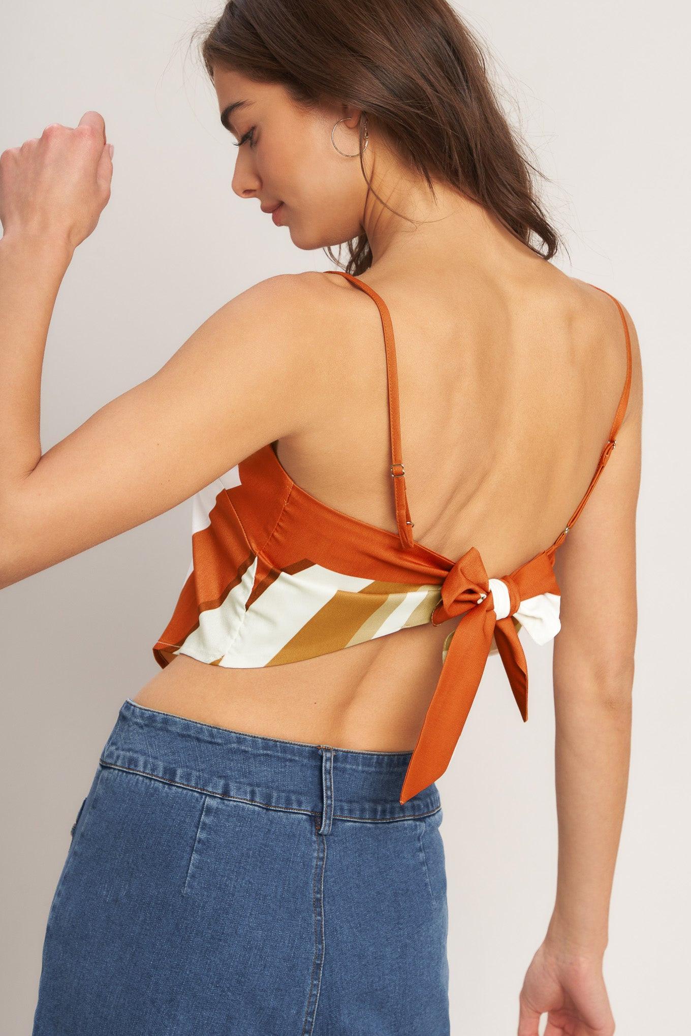 Woman wearing an orange top with a bow detail and blue pants on a plain background