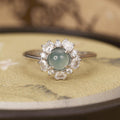 Elegant ring with a central green gemstone and diamond-like stones on a textured surface