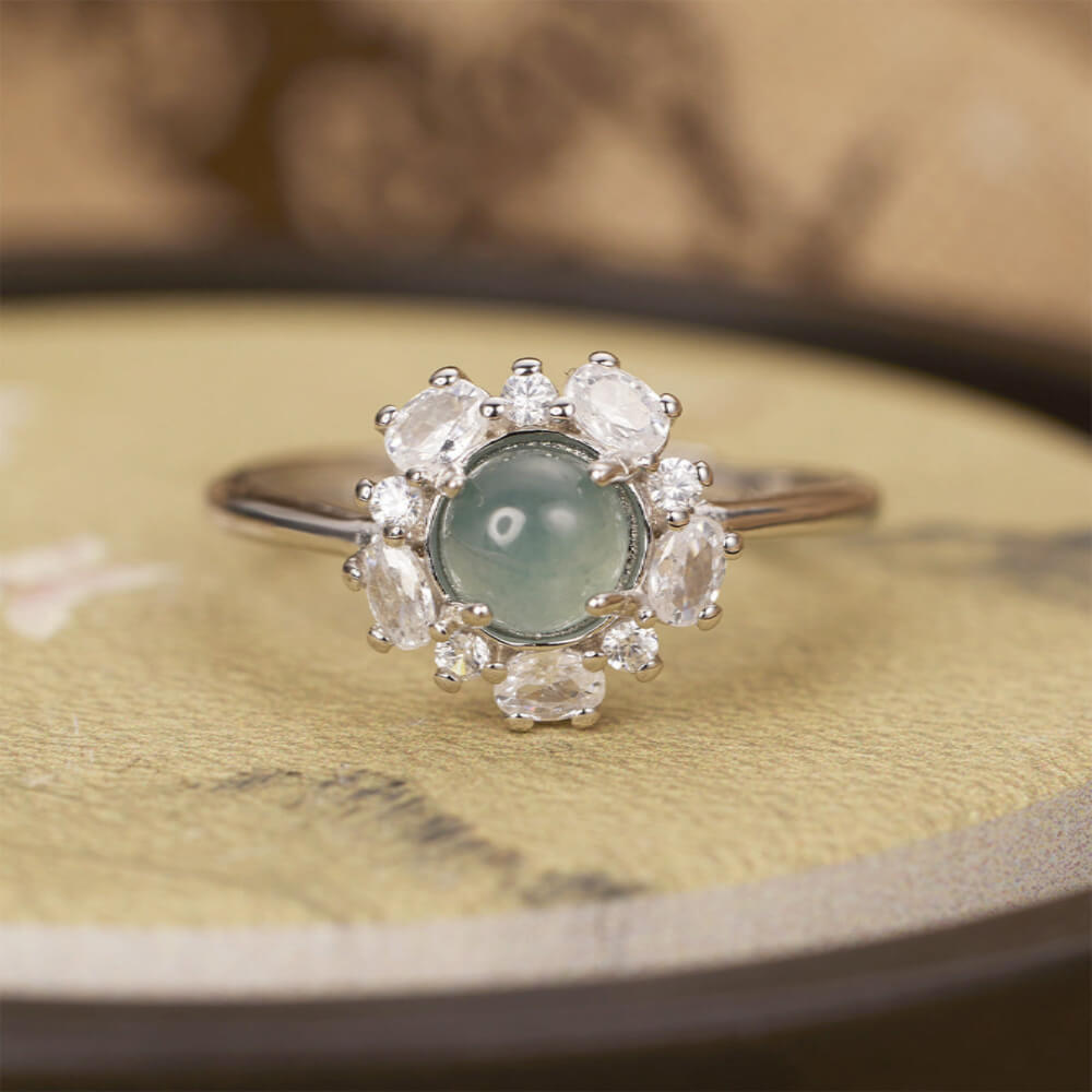 Elegant ring with a central green gemstone and diamond-like stones on a textured surface