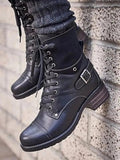 Black leather boots with buckles worn by a person against a stone wall.