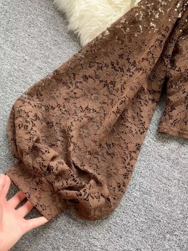 Brown lace fabric on a gray surface with a hand touching it