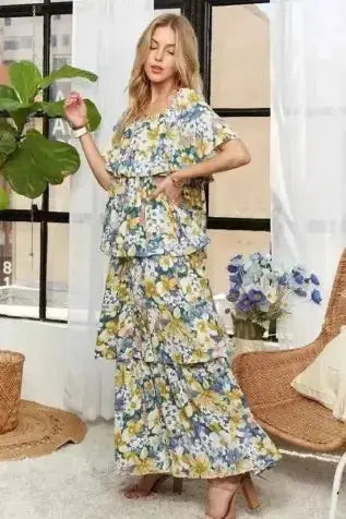 Woman in a floral dress standing in a room with a plant and chair.