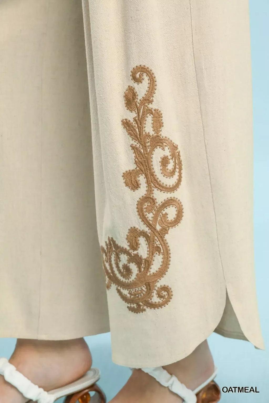 Beige pants with intricate gold embroidery on a light blue background