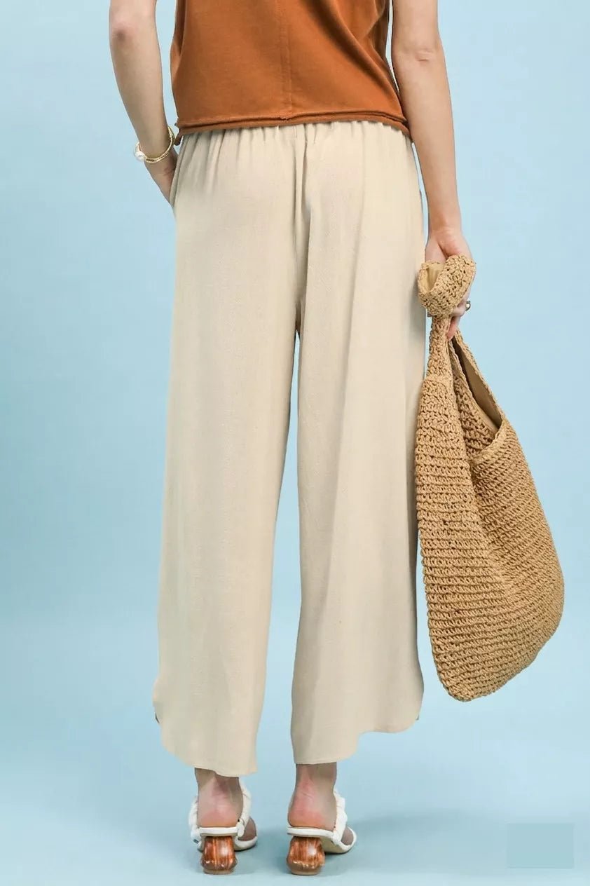 Person wearing beige pants and an orange top, holding a woven bag on a light blue background
