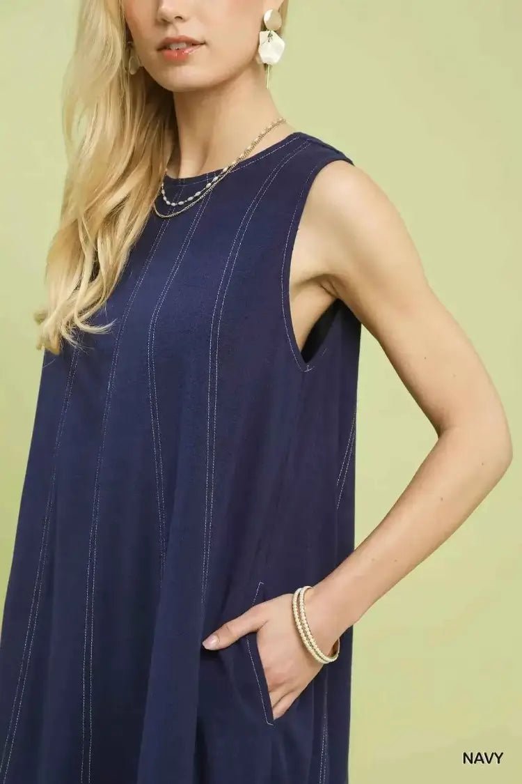 Woman wearing a navy sleeveless dress against a light green background