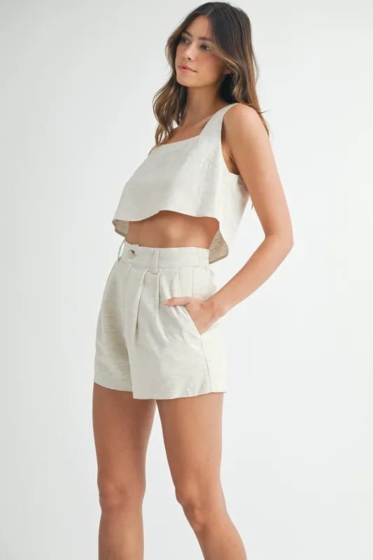 Woman wearing a white sleeveless top and beige shorts on a white background