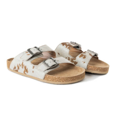 Pair of white sandals with brown cow print and wooden soles on a white background