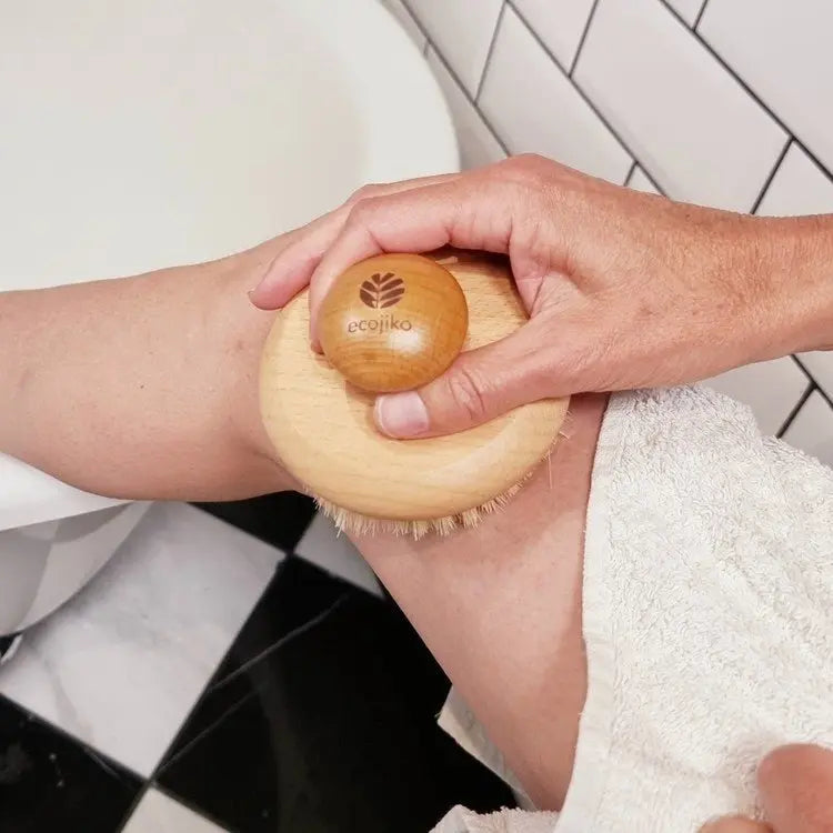 Person using round wooden body brush on forearm for bathroom exfoliation routine
