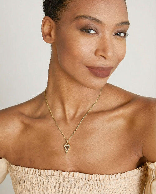 Woman wearing a gold necklace with a triangle pendant against a neutral background