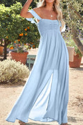 Woman wearing a light blue off-shoulder dress standing outdoors with plants and flowers in the background.