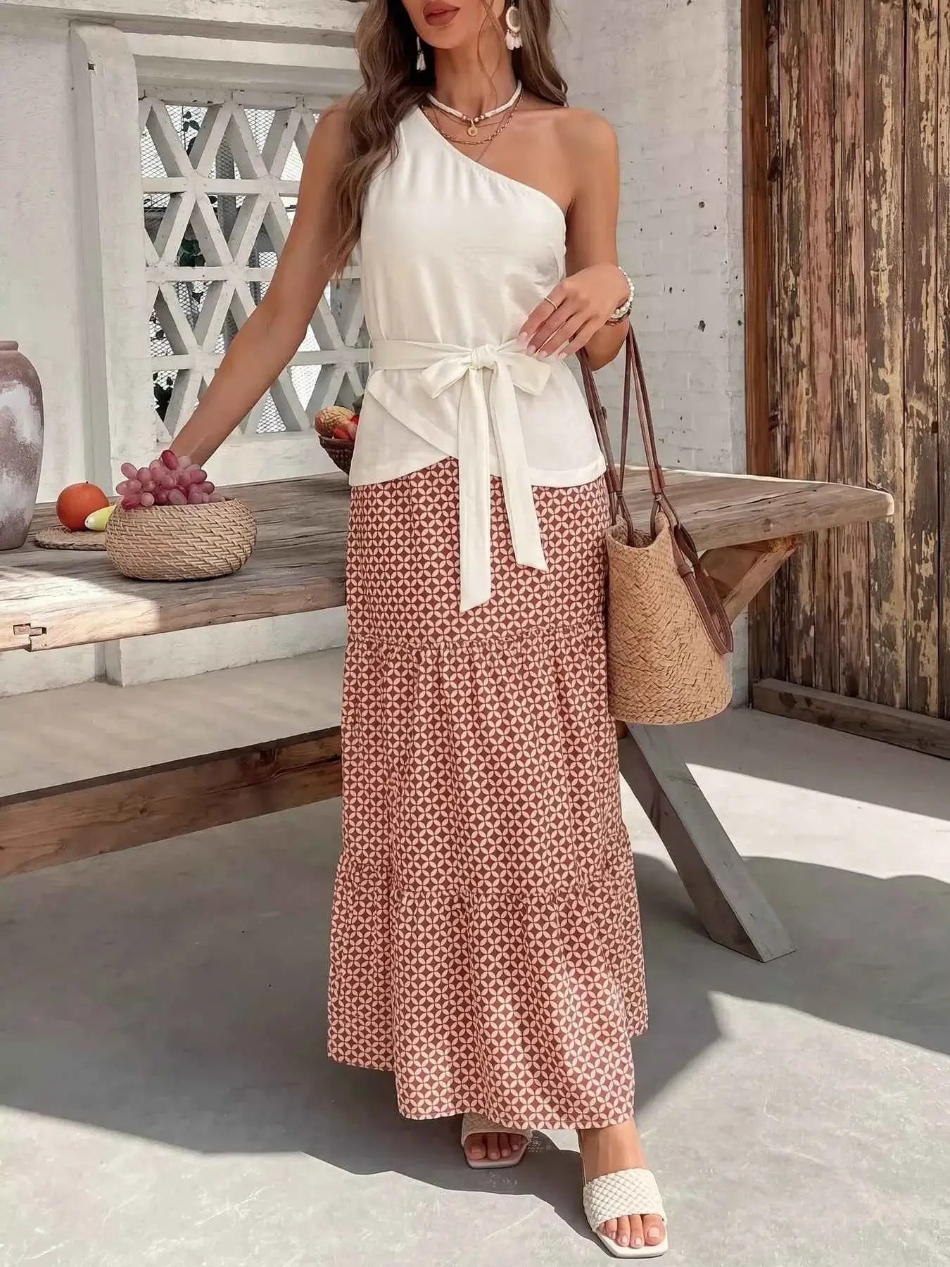 Woman in a white top and patterned skirt standing outdoors near a wooden table.