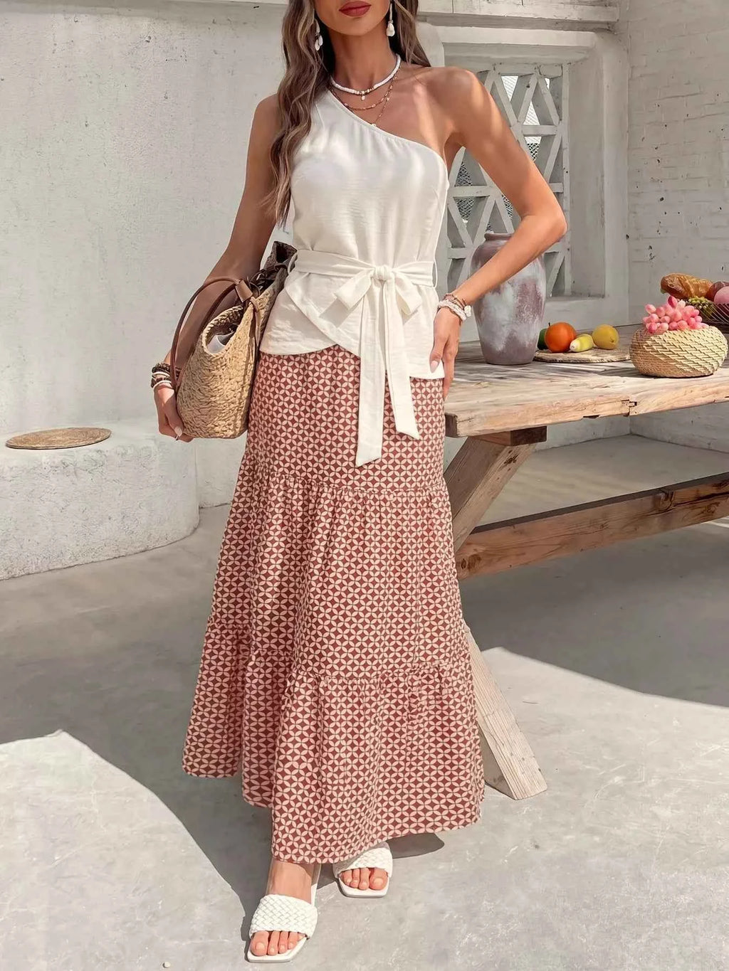 Woman in a white top and patterned skirt standing in a bright outdoor setting.