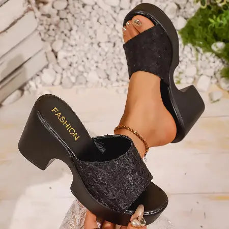 Black high-heeled sandals with 'FASHION' text worn by a person on a blurred natural background