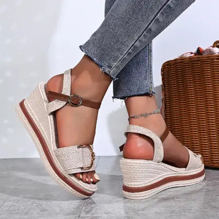 Beige wedge sandals with brown straps worn by a person on a light gray floor.