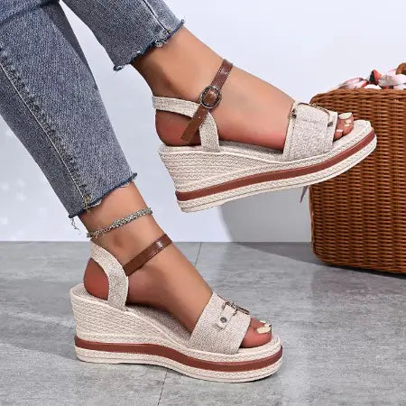 Woven wedge sandals with brown straps worn with jeans on a neutral background