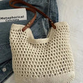 Beige crochet bag with brown handle on a light gray surface, next to denim jeans.