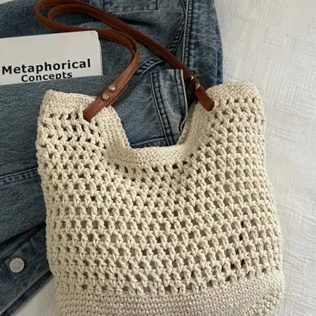 Beige crochet bag with brown handle on a light gray surface, next to denim jeans.