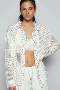 Woman wearing a white crochet top with floral patterns on a gray background