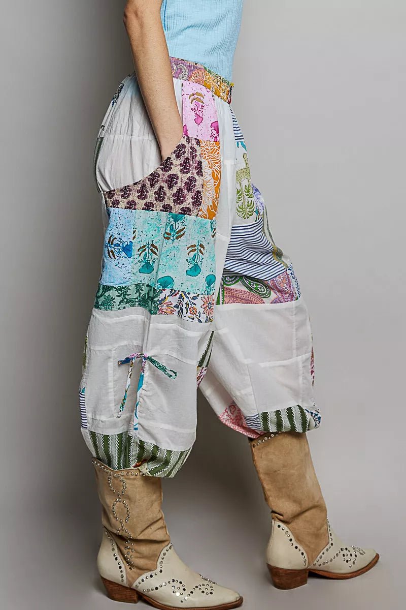 Person wearing colorful patchwork pants standing sideways with a plain background