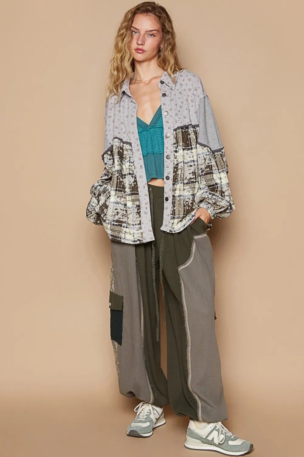 Woman wearing a patterned shirt, teal top, gray pants, and sneakers against a beige background