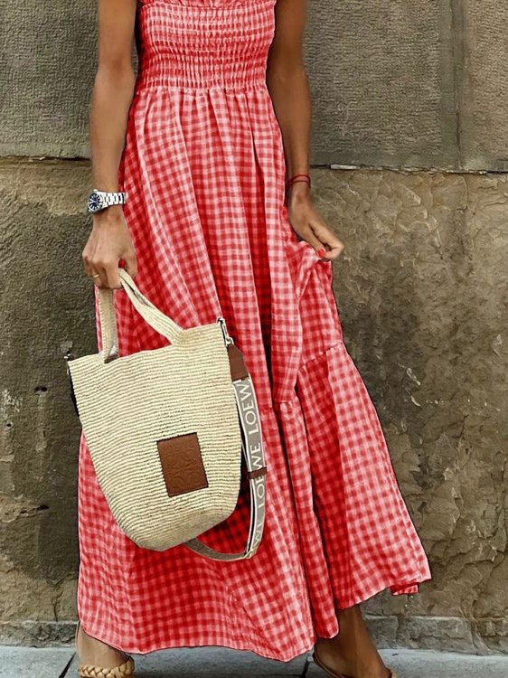 Person wearing a red checkered dress holding a straw bag against a stone wall.