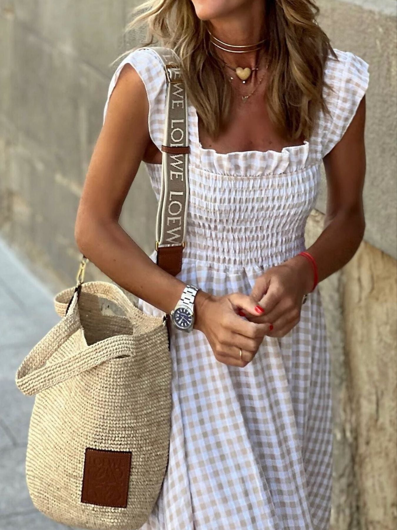Woman in a white checkered dress holding a straw bag against a neutral background