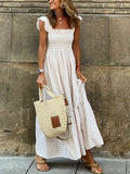 Woman in a white checkered dress holding a straw bag against a stone wall.
