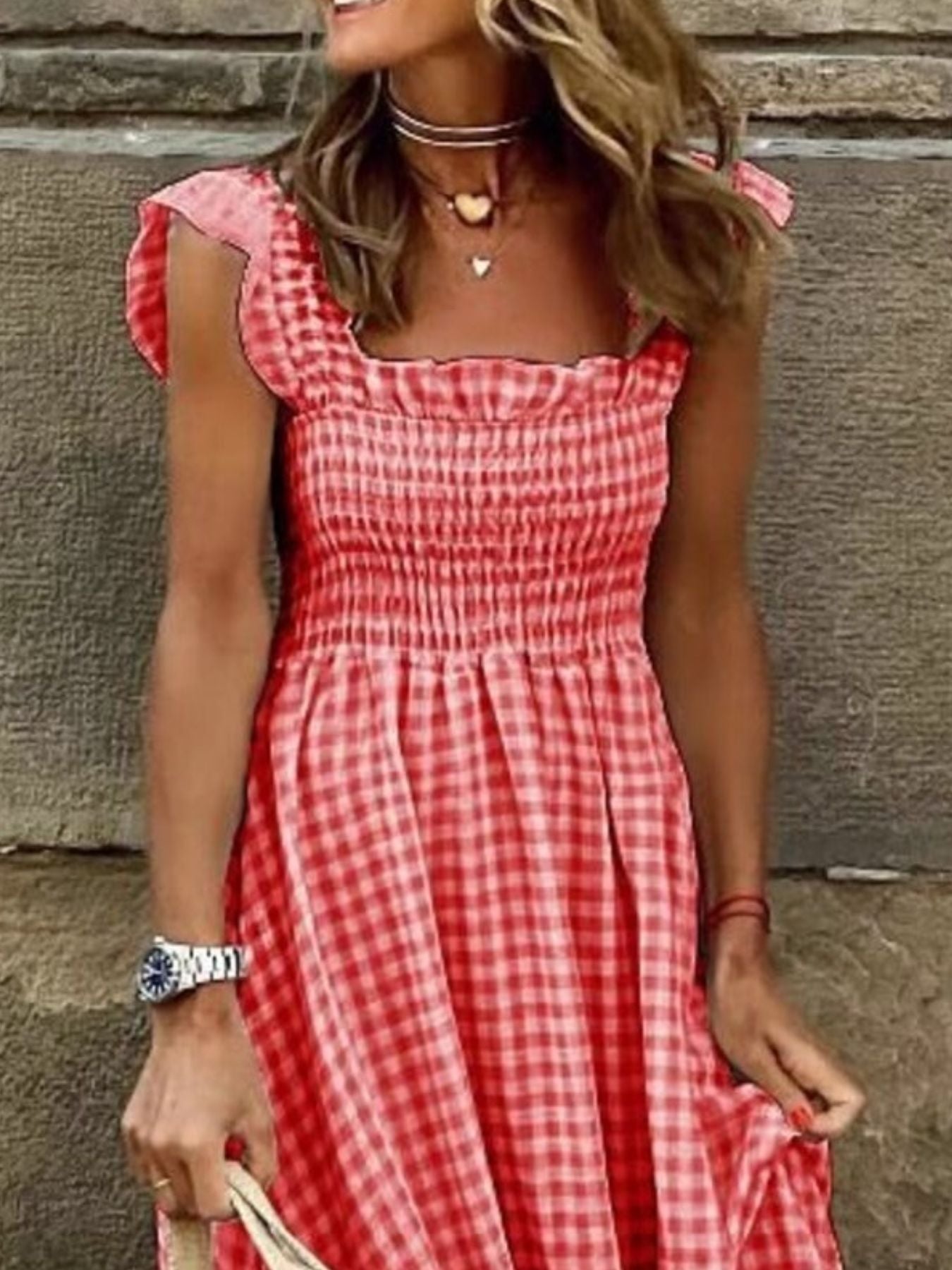 Woman wearing a red and white checkered dress against a stone wall.
