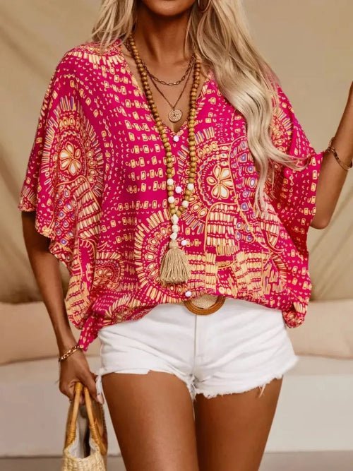 Woman wearing a bright pink and yellow patterned top with white shorts, holding a straw bag.