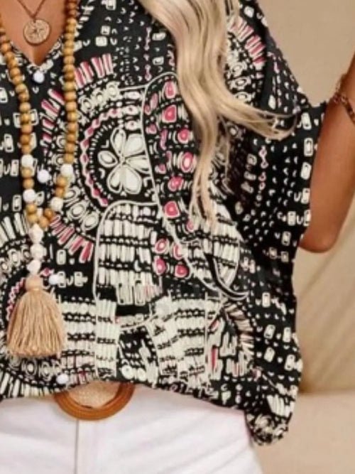 Person wearing a black patterned top with a tassel necklace