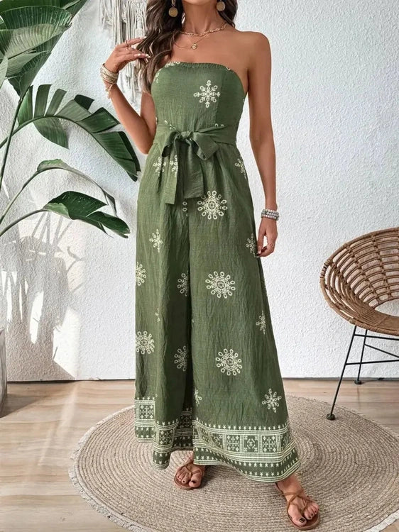Woman wearing a green strapless dress with white patterns in a room with a plant and chair.