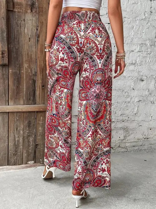 Person wearing a patterned wide-leg pants against a wooden and brick wall.