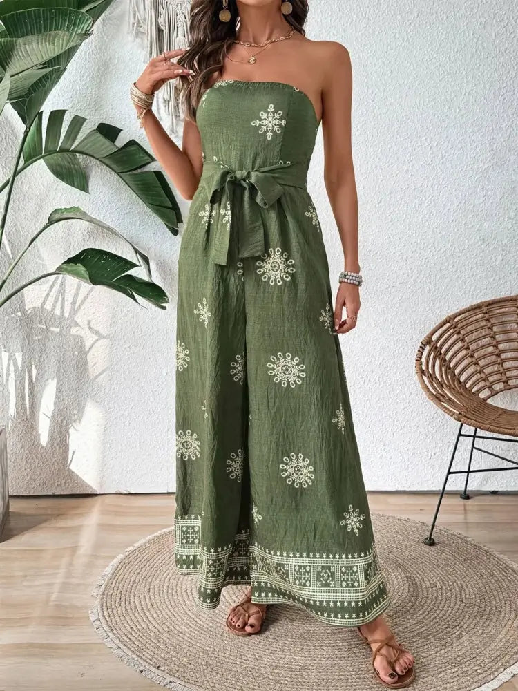 Woman wearing a green strapless dress with white patterns in a room with a plant and chair.