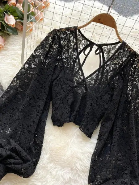 Black lace top on a hanger with a white textured surface and pink flowers in the background