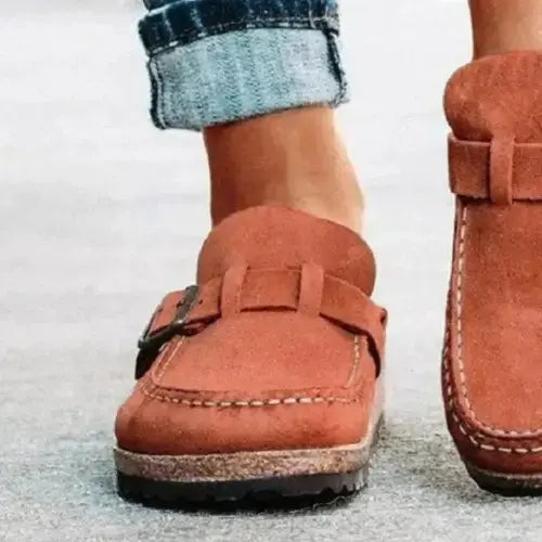 Brown suede loafers worn with rolled-up jeans on a light background