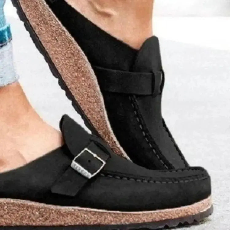 Black sandals with cork sole worn by a person on a light gray background