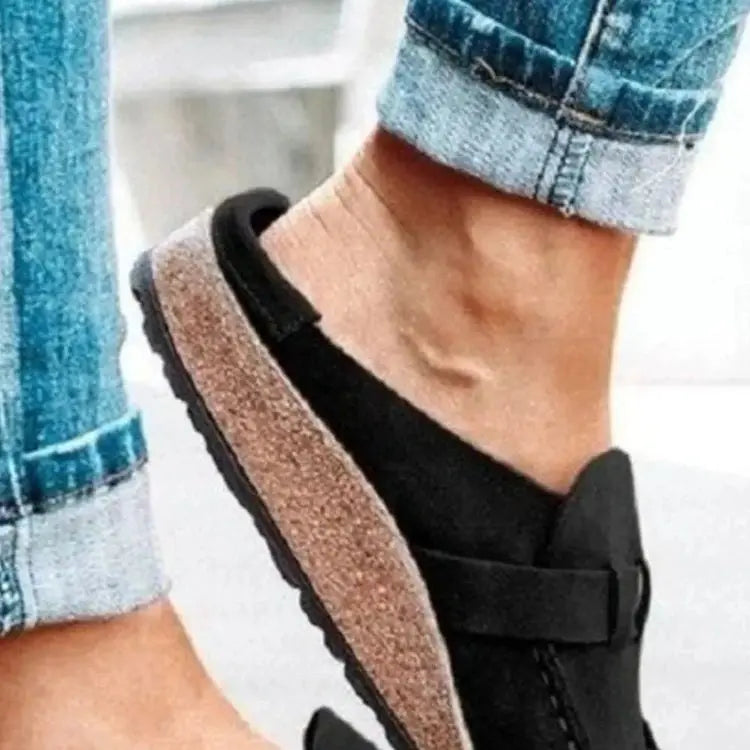 Black slip-on shoes worn with rolled-up jeans on a blurred background