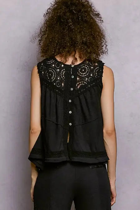 Person wearing a black sleeveless top with intricate lace details on a plain background