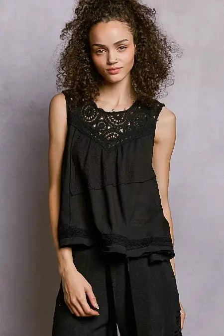 Woman wearing a black sleeveless top with lace details against a gray background