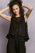 Woman wearing a black sleeveless top with lace details against a gray background