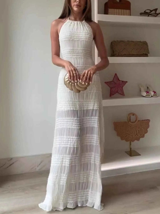 Woman in a white halter neck dress holding a gold clutch in a room with shelves.