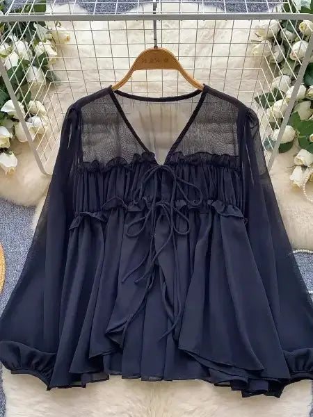 Black blouse with sheer panels on a hanger against a decorative background