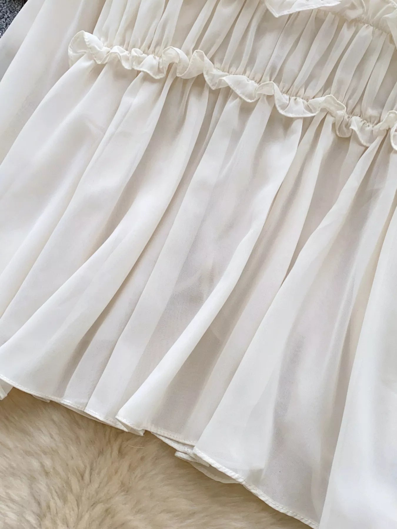 Close-up of a white skirt with ruffled waistband on a textured surface