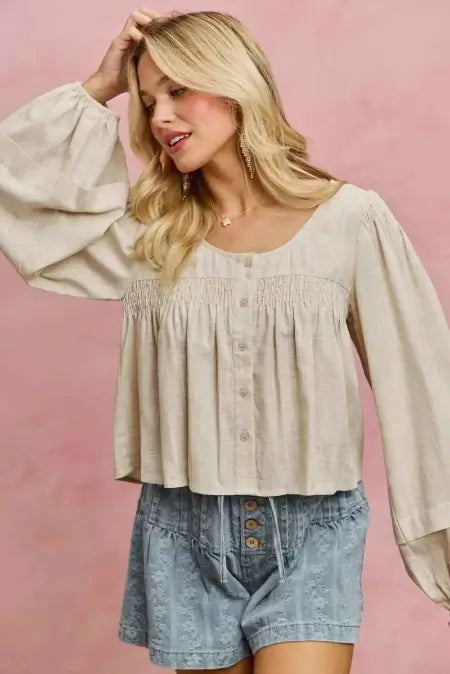 Woman wearing a beige blouse and denim shorts against a pink background