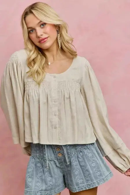 Woman wearing a beige blouse and denim shorts against a pink background