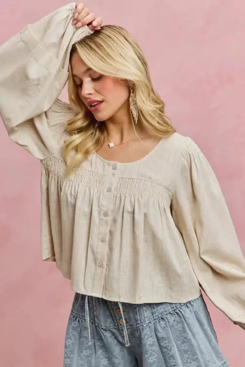 Woman wearing a beige blouse with long sleeves against a pink background